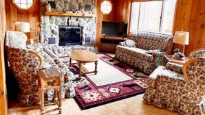 Una sala de estar acogedora con chimenea de piedra, muebles con estampado floral y un ventanal grande.