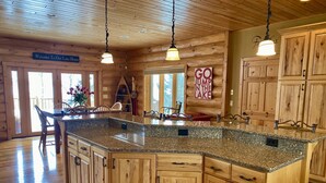 A wooden cabin interior with a kitchen island, wooden cabinets, and a sign that reads "Welcome To Our Lake Home".