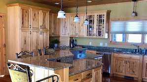 A spacious kitchen with wooden cabinets, granite countertops, and pendant lighting.