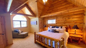 A log cabin bedroom with a large bed, a sofa, and a window with a view of the lake.