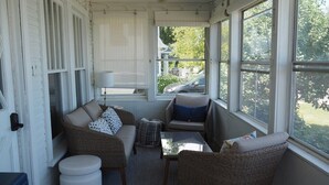 A sunroom with wicker furniture, a small table, and a view of the outdoors. - The Bright and Breezy - Lakefront with Spa! (Frankfort)