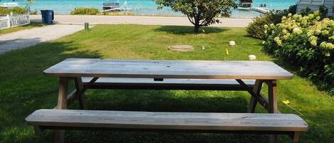 A picnic table in a grassy area with a view of a lake and boats in the background.