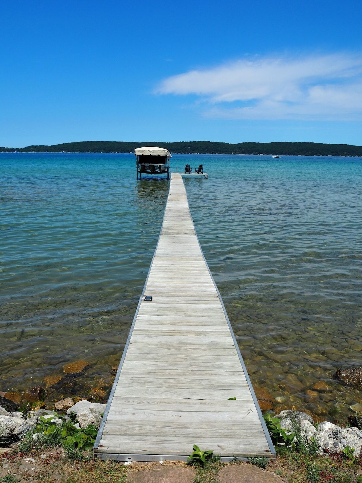 A wooden pier extending into a calm lake with a covered structure at the end.