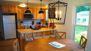 A kitchen with wooden cabinets, a central island with seating, a dining table, and a view of the outdoors. - The Bright and Breezy - Lakefront with Spa! (Frankfort)