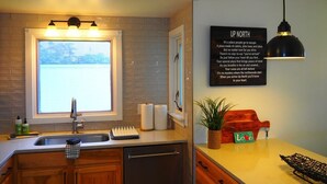 A modern kitchen with a large window, a sink, and a countertop. There is a sign on the wall that reads "UP NORTH". - The Bright and Breezy - Lakefront with Spa! (Frankfort)