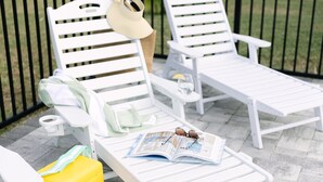 Two white lounge chairs with a magazine, a yellow bag, and a hat on one of them.