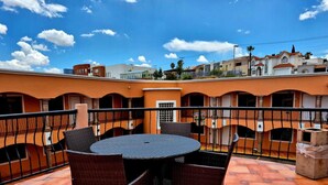 A rooftop terrace with a round table and wicker chairs, surrounded by orange walls and a tiled floor.