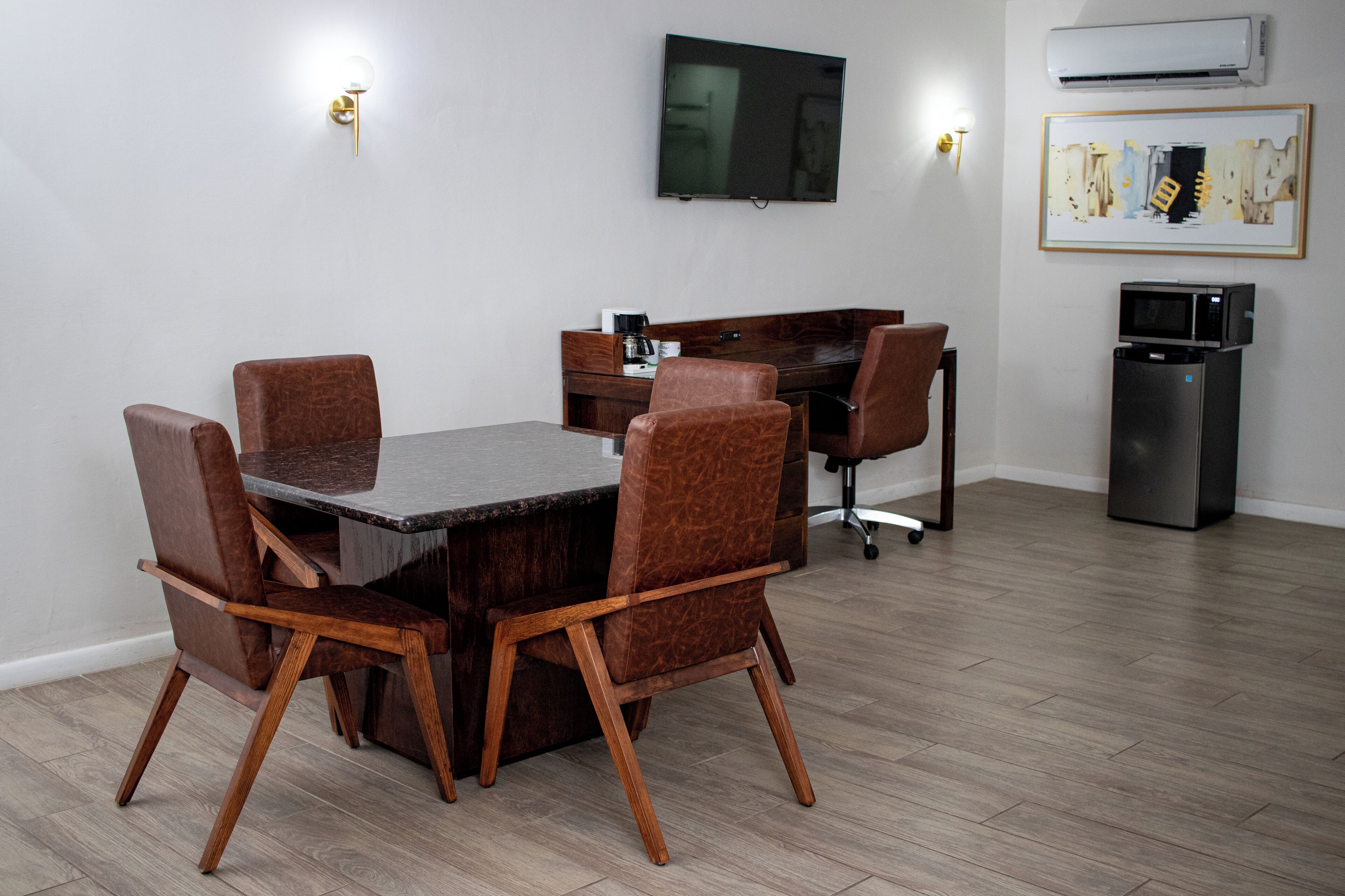 A dining area with a table and chairs, a flat-screen TV, a coffee machine, and a refrigerator.