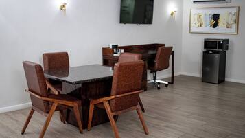 A dining area with a table and chairs, a flat-screen TV, a coffee machine, and a refrigerator.