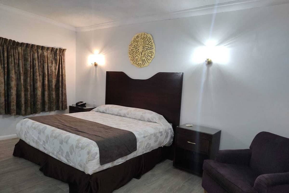 Una habitación de hotel con cama, mesitas de noche, una silla y luces en la pared.