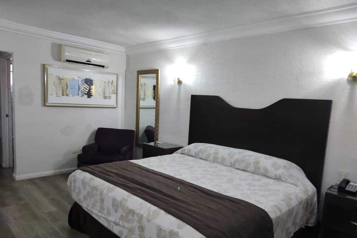 Una habitación de hotel con una cama grande, una silla, un escritorio y un espejo.