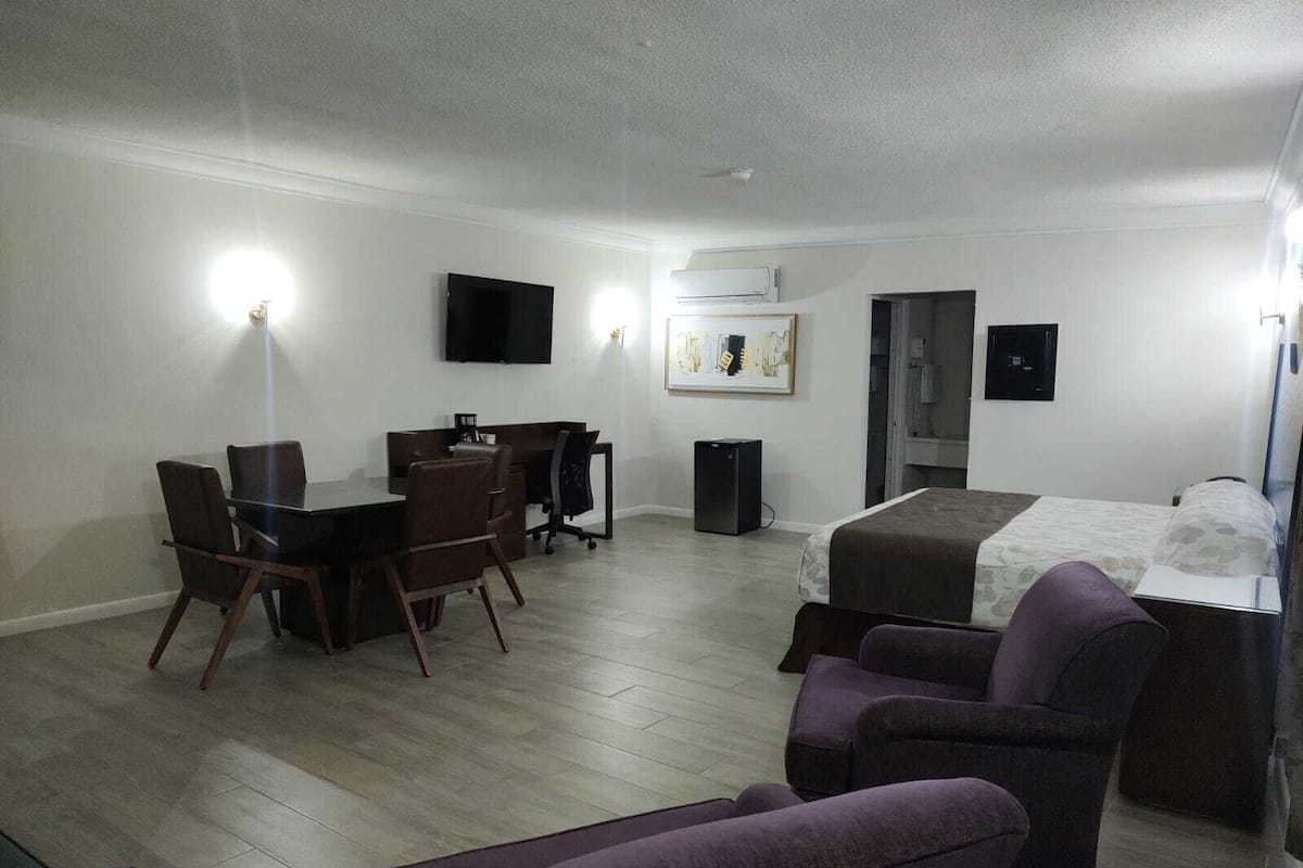 Una habitación de hotel con una cama, un escritorio con una silla, un televisor y un equipo de aire acondicionado pequeño.