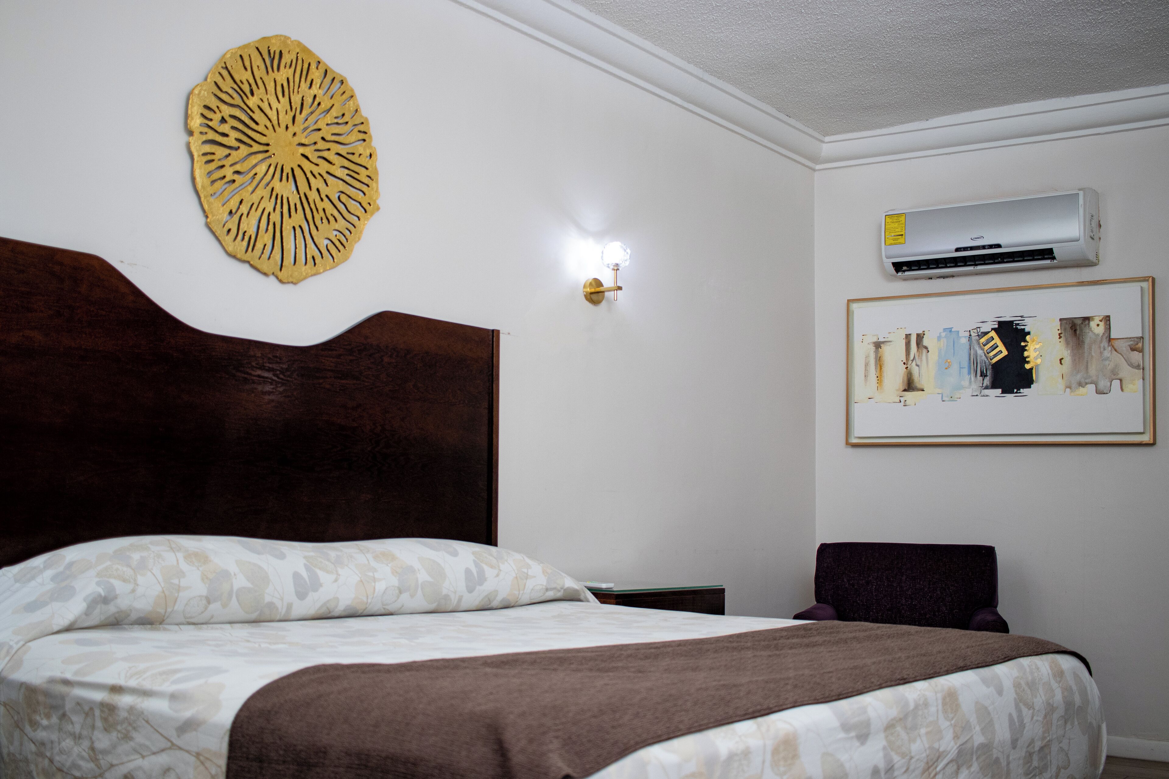 Une chambre d’hôtel comprenant un lit, un climatiseur fixé au mur, une œuvre d’art encadrée et un élément décoratif mural.
