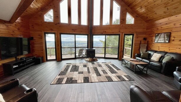 A spacious living room with a large TV, a fireplace, and a view of the outdoors through large windows.