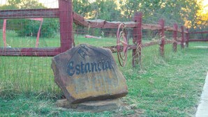 A rustic stone sign with the name 'Estancia' in a rural setting with a wooden fence and a metal gate. - Modern Private Cabin, Fishing, Shooting Range, Fire Pit, 4WD Trails & Canoeing (Bridgeport)