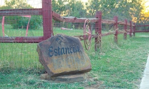 Un cartello in pietra rustica con la scritta 'Estancia', in un contesto rurale con una recinzione in legno e un cancello in metallo.