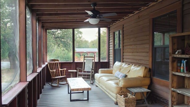 A covered porch with a wooden ceiling, a ceiling fan, a leather sofa, a rocking chair, a wooden table, and a view of the outdoors. - Modern Private Cabin, Fishing, Shooting Range, Fire Pit, 4WD Trails & Canoeing (Bridgeport)