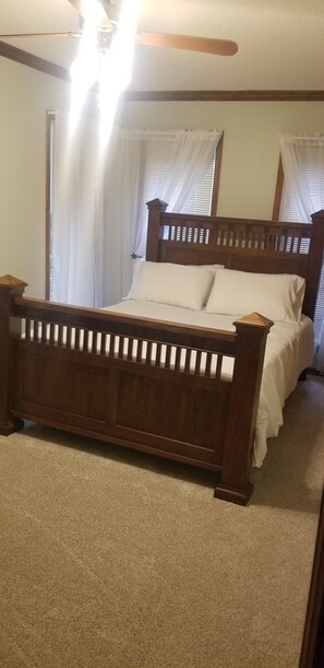A bedroom with a wooden bed frame, white bedding, and a ceiling fan.