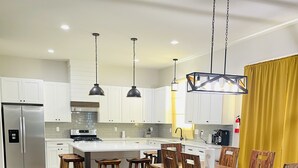 Eine moderne Küche mit weißen Schränken, einem Edelstahl-Kühlschrank, einer zentralen Kochinsel mit Sitzgelegenheiten und Pendelleuchten.