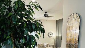 Ein modernes Wohnzimmer mit einer großen Kübelpflanze, zwei Sofas, einem Deckenventilator und einem Wanddekor.
