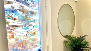 Una puerta con un vitral, un espejo y una planta en maceta sobre un pedestal.