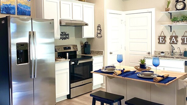 Una cocina moderna con electrodomésticos de acero inoxidable, armarios blancos y una isla central con taburetes.
