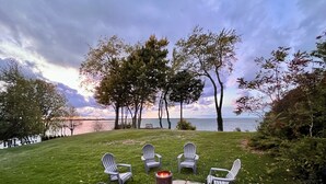 Une terrasse avec quatre fauteuils Adirondack et un foyer, donnant sur une étendue d’eau et des arbres.