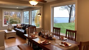 Un coin repas avec une table en bois dressée pour le repas, de grandes fenêtres donnant sur un lac et des arbres, et un ventilateur de plafond au-dessus.