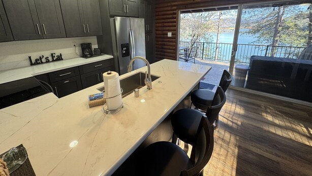 A modern kitchen with grey cabinets, a marble island, and a view of the lake. - Lakefront #1 Cabin on Acre, Kayaks, Paddle Boards  - Shasta Lakeshore Retreat #4 (Lakehead)