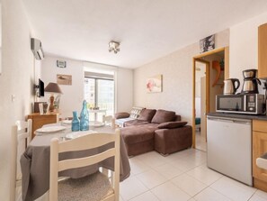 Un espace de vie compact comprenant un coin repas, un canapé, une kitchenette et une fenêtre laissant entrer la lumière naturelle.