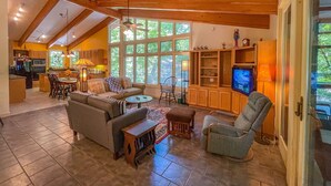 A spacious living area with a high ceiling, wooden beams, a kitchen in the background, and large windows offering a view of the outdoors. - On the Chattahoochee River-Walk to Downtown Alpine Helen (Helen)