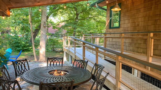An outdoor patio with a round table and chairs, surrounded by a wooden deck and a view of trees. - On the Chattahoochee River-Walk to Downtown Alpine Helen (Helen)