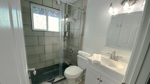 Et moderne badeværelse med bruseniche, toilet og vask med spejl over.