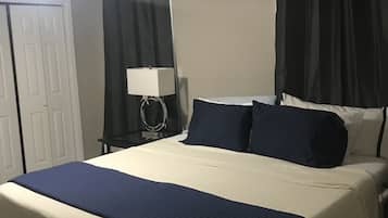 A hotel room with a bed, a nightstand, a lamp, a ceiling fan, a door, and black curtains.
