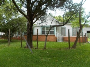A house with a brick foundation and a white exterior, surrounded by a grassy yard and trees. - Nice & Spacious House in Silsbee w/ Self Check-in (Silsbee)