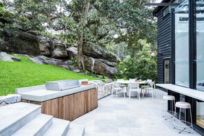 An outdoor patio with a stone bench, a wooden table, and a glass-enclosed area with a bar. - Crane Lodge (Palm Beach)