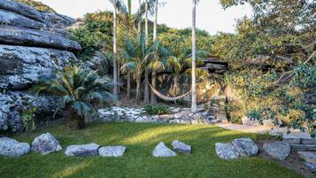 Un jardín con palmeras, rocas y una hamaca.