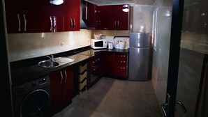 Une cuisine de taille réduite avec des meubles de rangement rouges, un four à micro-ondes, un grille-pain et un réfrigérateur.