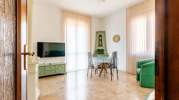 A living room with a television, a dining table with chairs, a green sofa, and a cabinet.