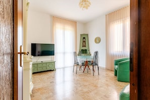 A living room with a television, a dining table with chairs, a green sofa, and a cabinet.