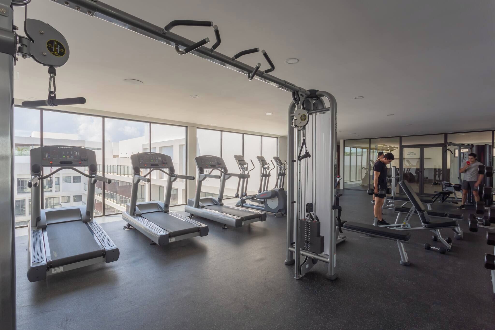 A gym with treadmills, weight machines, and a large window offering a city view.