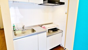A compact kitchen with white cabinets, a stainless steel sink, and a black range hood. - Rave K 201 (Naha)