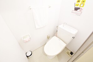 A small, clean bathroom with a toilet, a sink, and a trash bin. There are hand sanitizer dispensers and a towel hanging on the wall. - Rave K 201 (Naha)