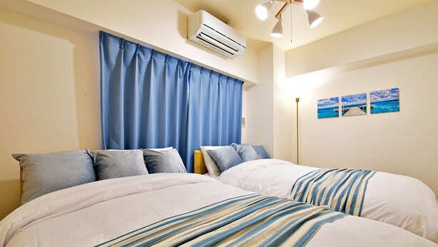 A double bed with striped bedding, a ceiling fan, and an air conditioning unit. - Rave K 201 (Naha)