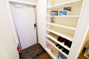 A hallway with a white door, a fire extinguisher, and a shoe rack with multiple shelves. - Rave K 201 (Naha)