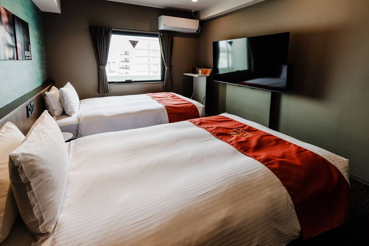 A hotel room with two beds, a TV, and a window with curtains.