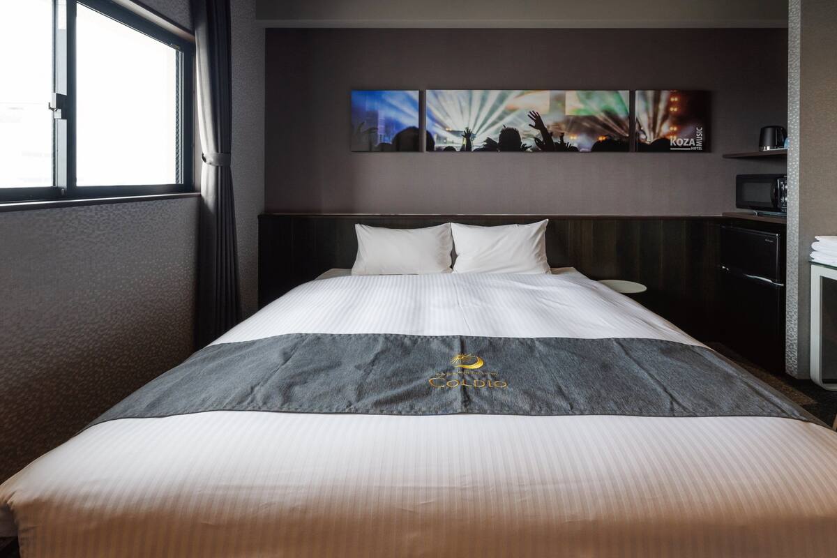 A hotel room with a large bed, a nightstand, a TV, and a window.