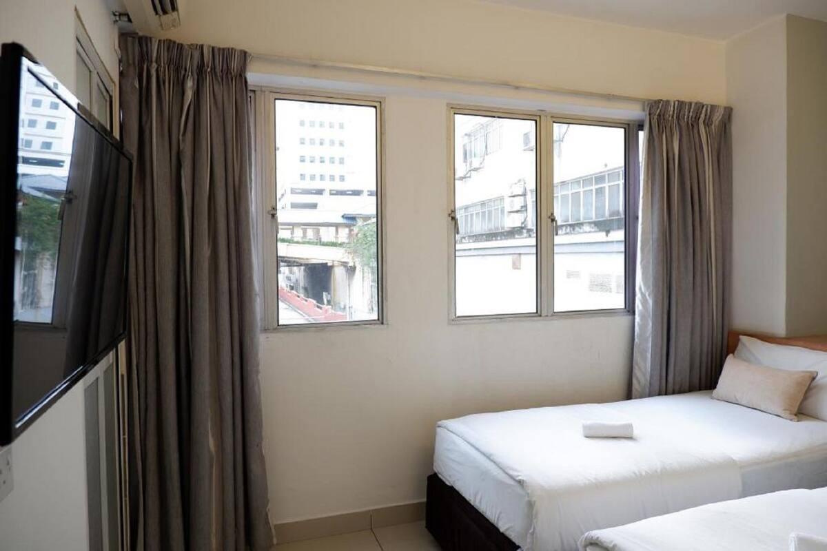 Habitación de hotel con dos camas, televisión y ventanas amplias con cortinas.