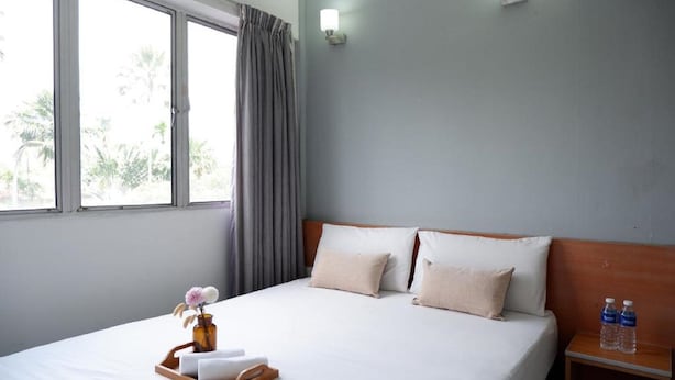 A hotel room with a bed, a bedside table with water bottles, a tray with towels and a vase of flowers, and a window with curtains. - Indah Garden Hotel (Ampang)