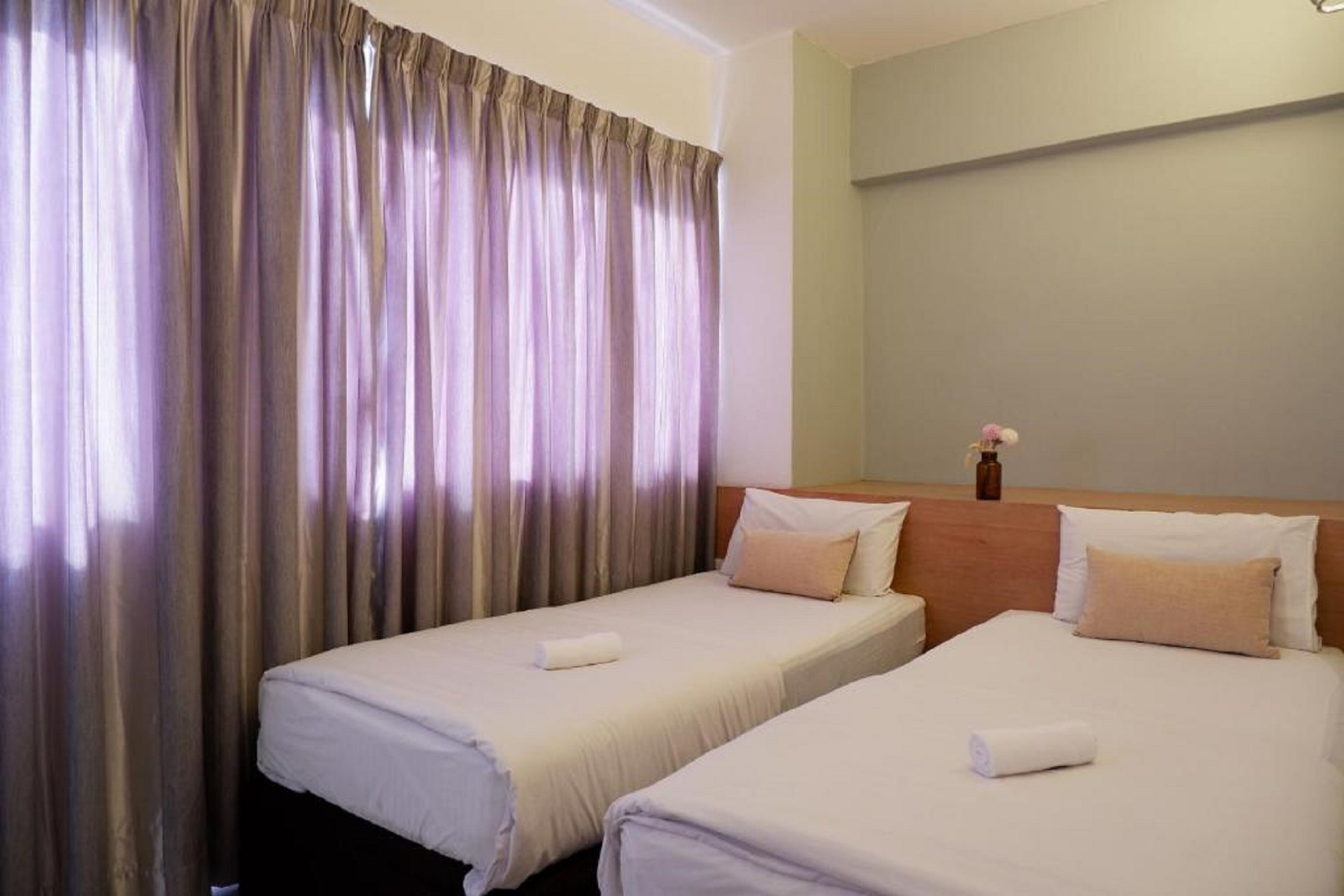A hotel room with two single beds, beige bedding, a wooden headboard, and a large window with curtains.